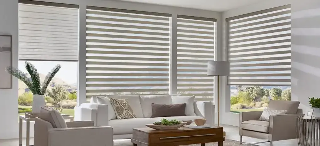 Living room with white sofa, chairs, blinds, and a view of trees through the windows.