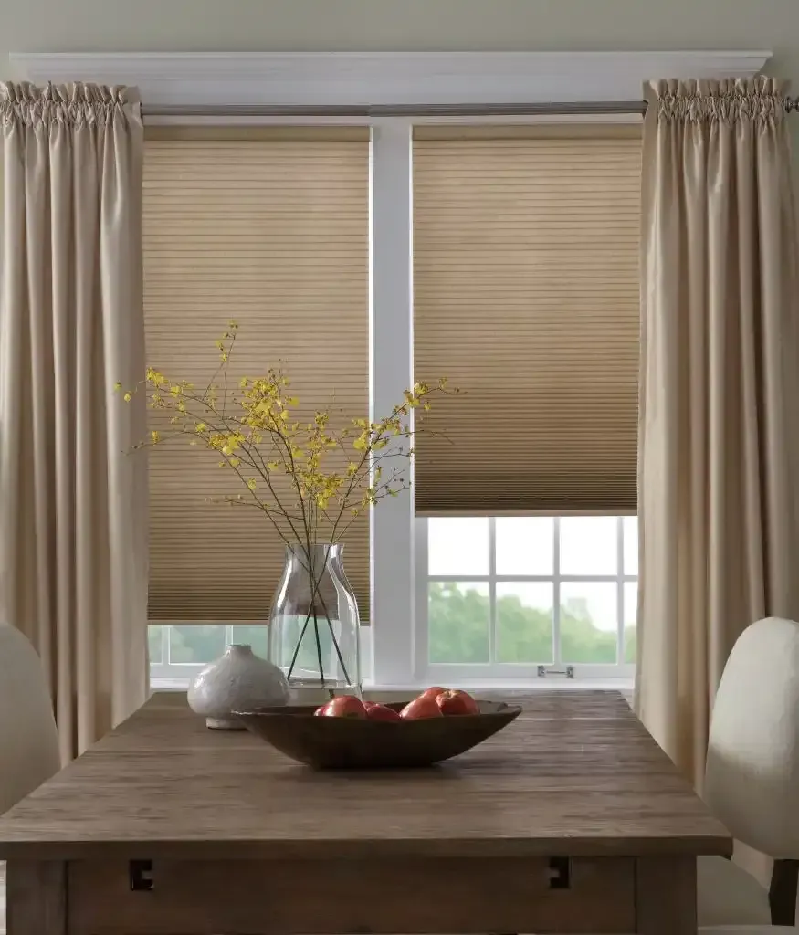 Dining room with table, window blinds, curtains, and floral arrangement.