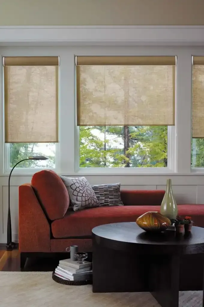 Living room with a red couch, round coffee table, and windows with beige roller shades.