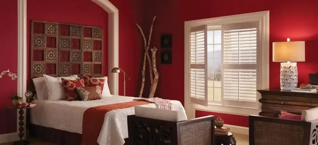 Bedroom with red walls, bed, window with shutters, and decorative accents.