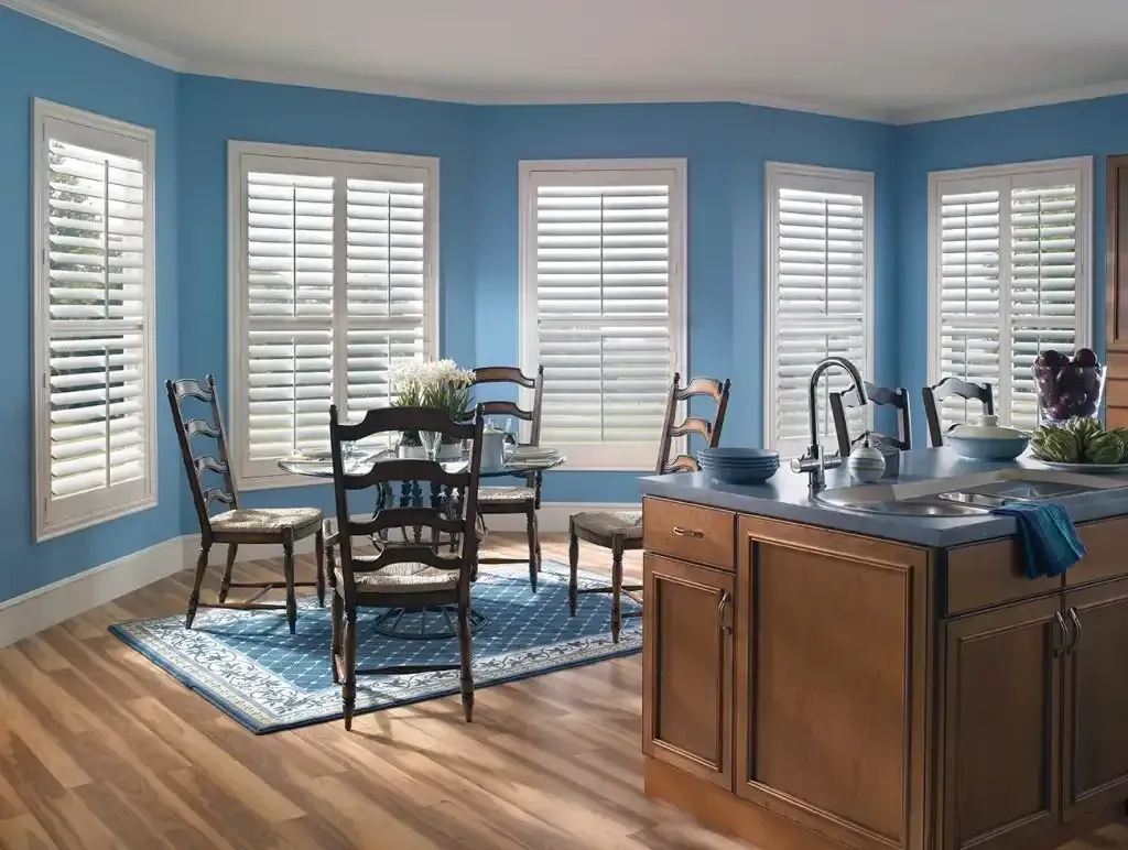 A bright blue dining room with white shutters, wooden floors, and a kitchen island.