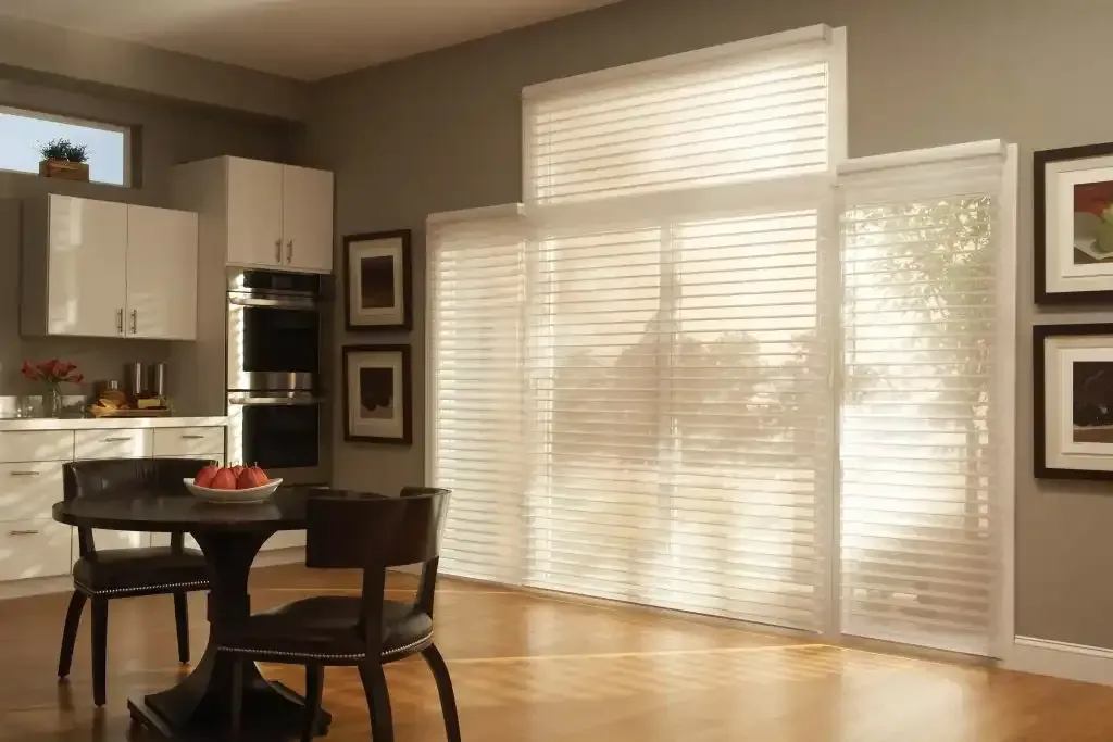 Kitchen with round table, chairs, large window with blinds, and white cabinets.